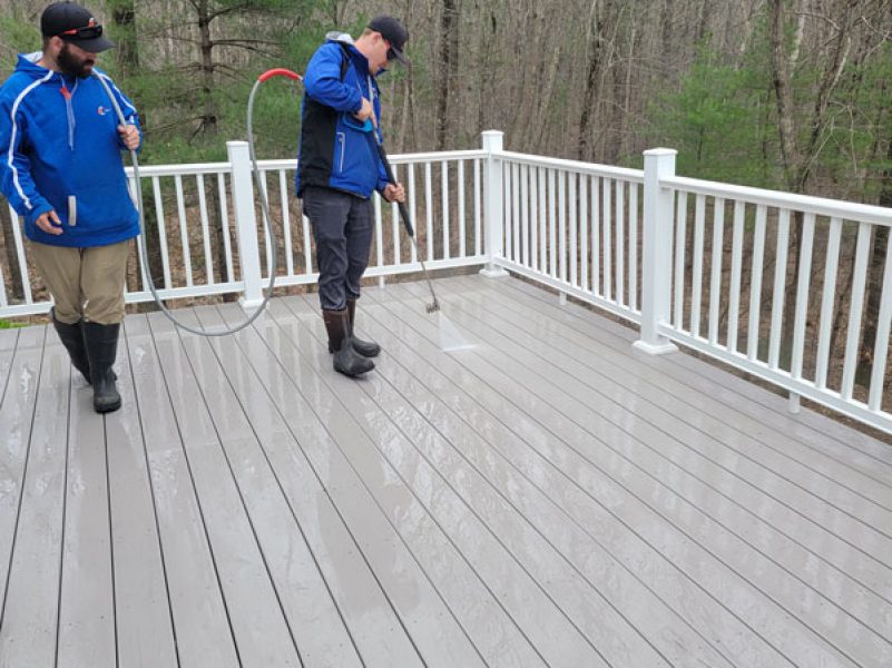 professionals in blue work jackets pressure washing deck